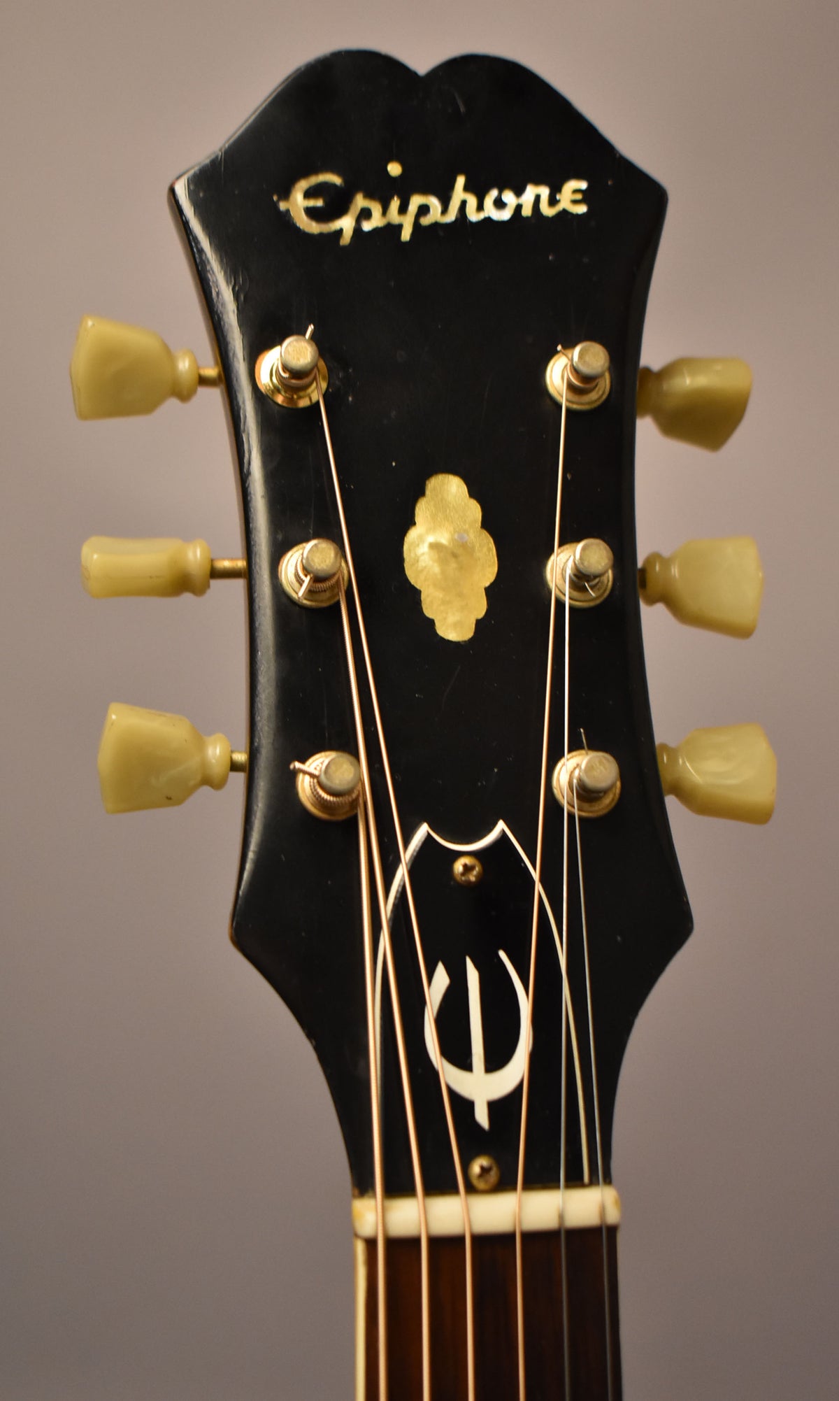 Close-up of the black headstock with gold Epiphone logo, gold tuners with cream buttons, and a decorative gold inlay.