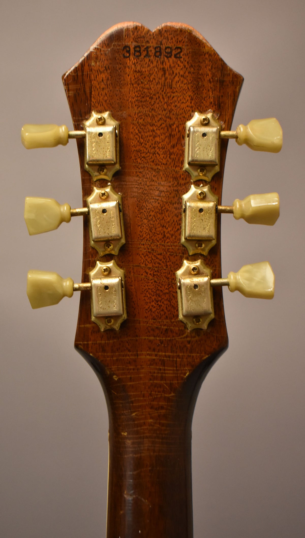 The back of the headstock and upper neck, showing six gold tuners with cream buttons, and wear to the dark wood finish.