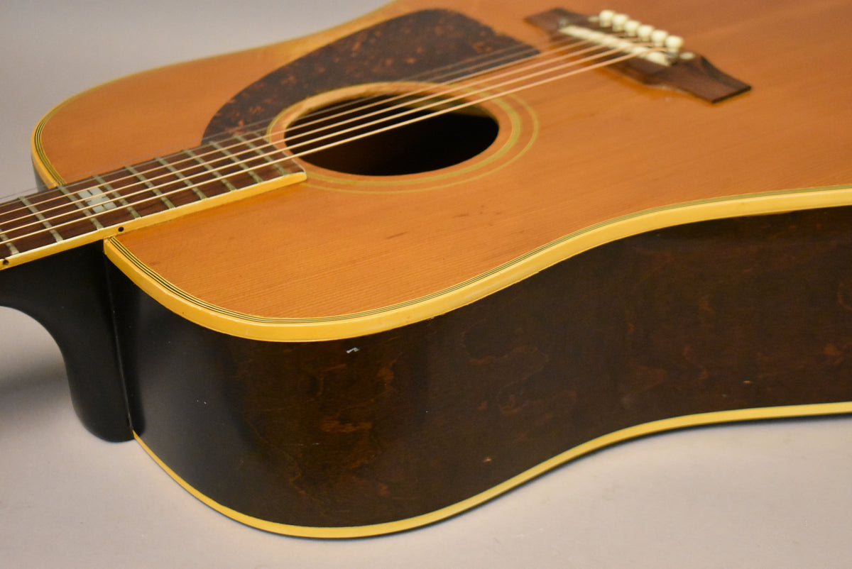 Upper body of a natural finish acoustic guitar, showing the dark brown sides, pickguard, soundhole, bridge, and fretboard.