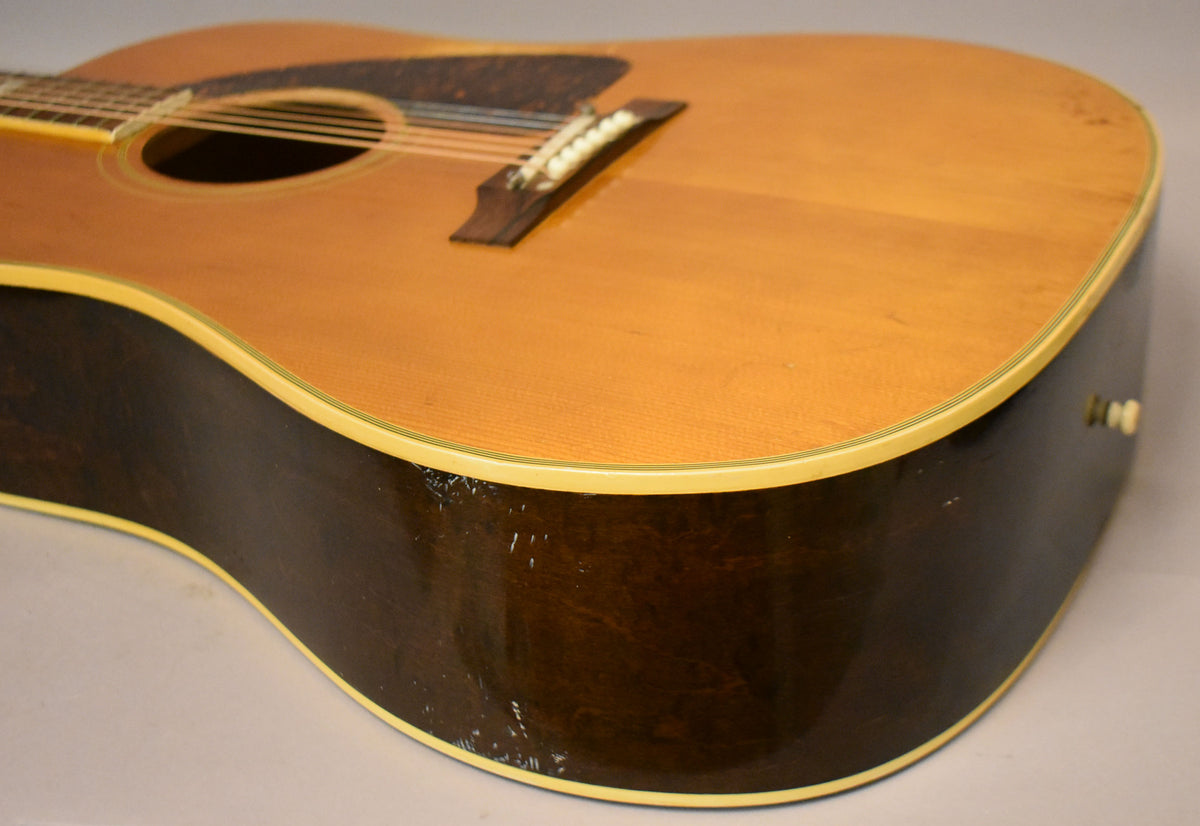 The lower bout of a natural finish acoustic guitar, showing a dark brown side with significant finish wear and binding.