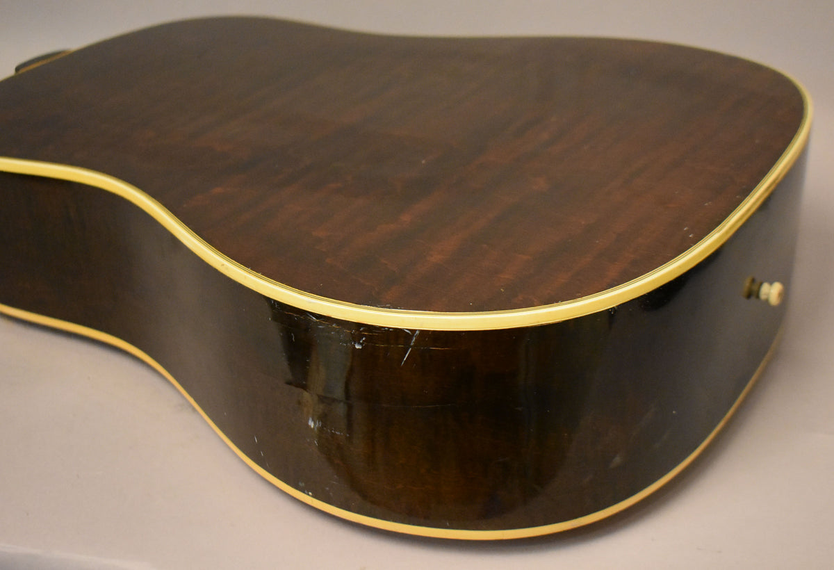 The lower bout of the guitar, showing the dark brown back and side with cream binding and visible scratches and wear.