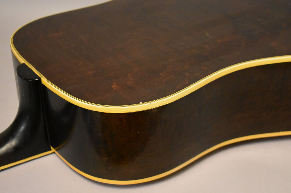 Close-up of the guitar's lower bout and neck heel, showing the dark brown body with cream binding and a small chip on the top edge.