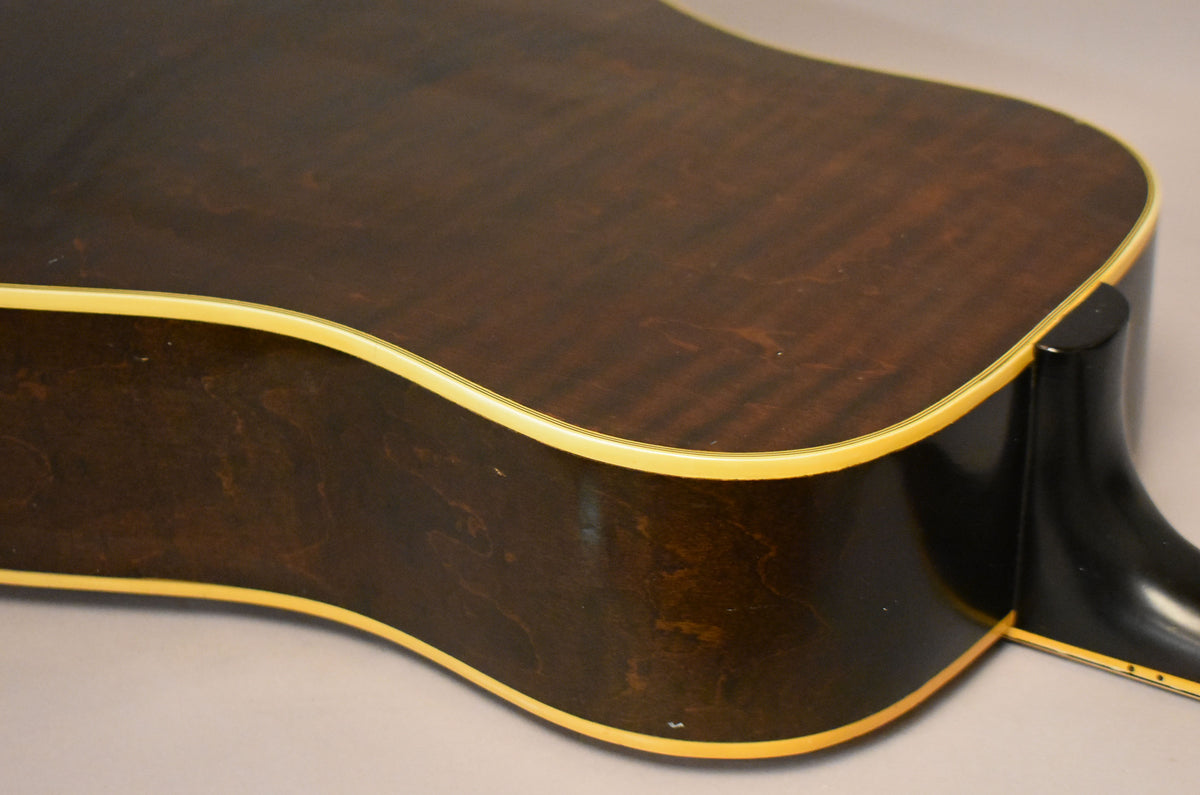 The guitar's dark brown back and side are visible, with cream binding and a black neck heel, showing minor wear on the lower bout.