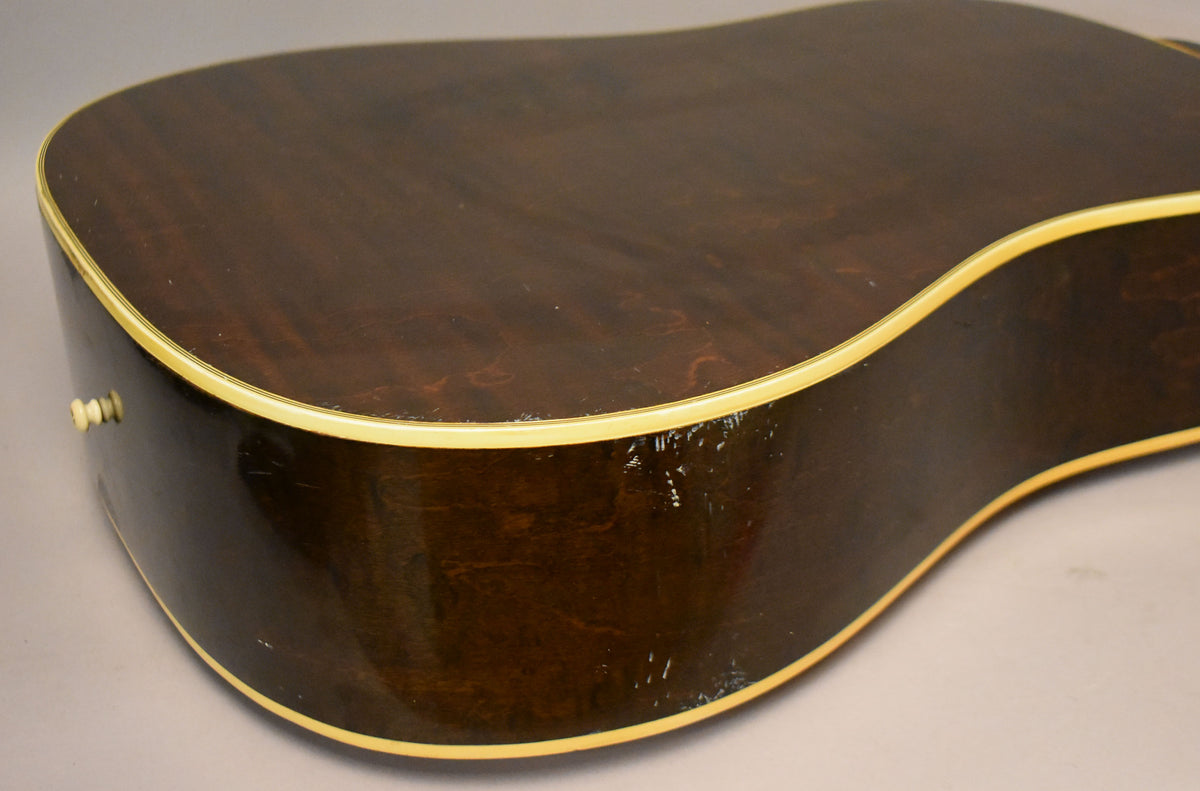 The guitar's dark brown back and side are visible, with cream binding, a strap button, and notable finish wear and scratches.