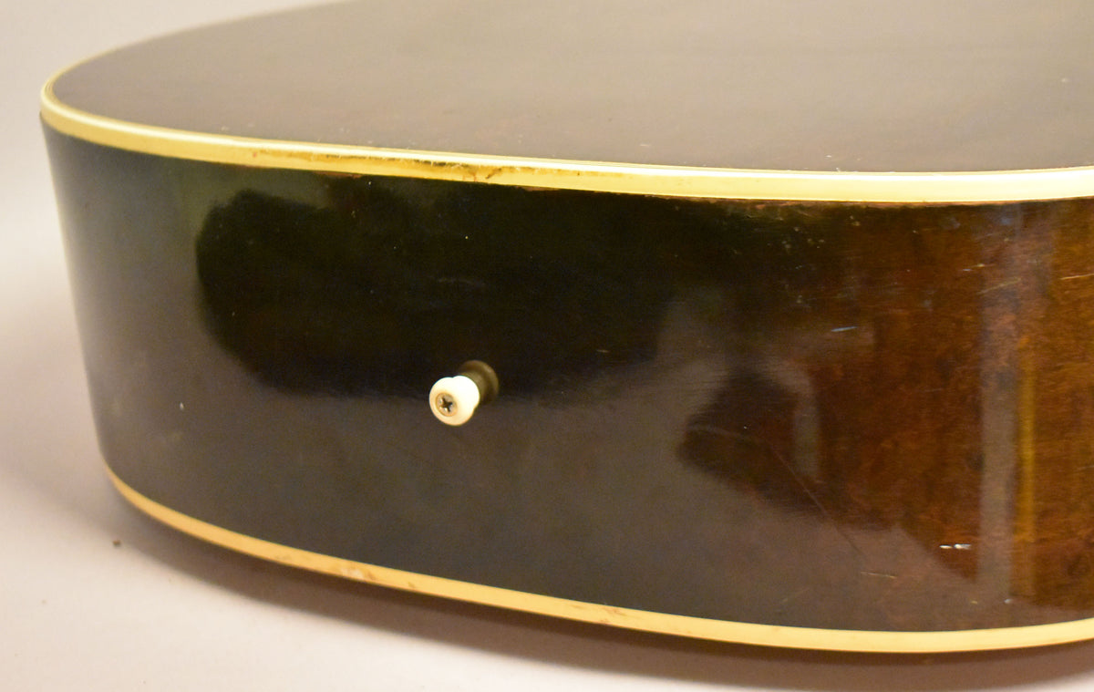 Close-up of the guitar's lower bout, showing the dark brown back and side with a cream binding and a white end pin.