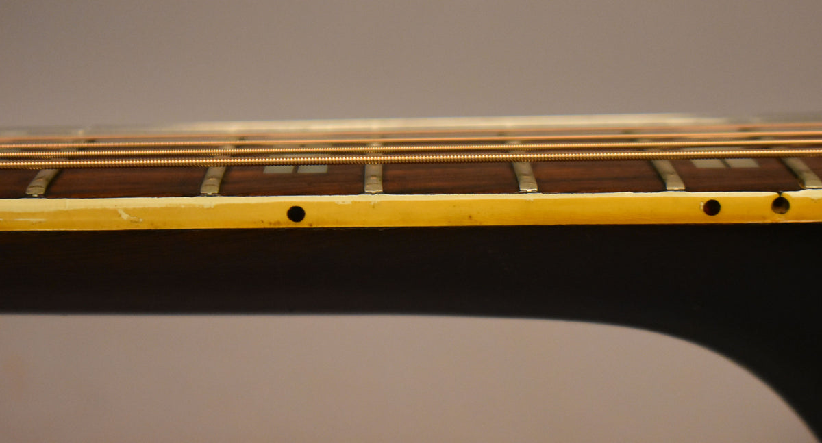 Close-up of the guitar's dark fretboard and light binding, showing two holes on the side and some wear on the binding.