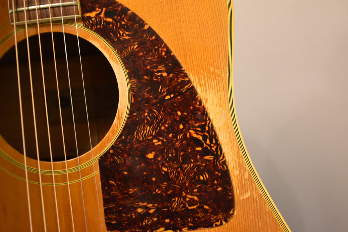 Close-up of the natural finish acoustic guitar's body, showing the soundhole, strings, tortoiseshell pickguard, and light finish wear.