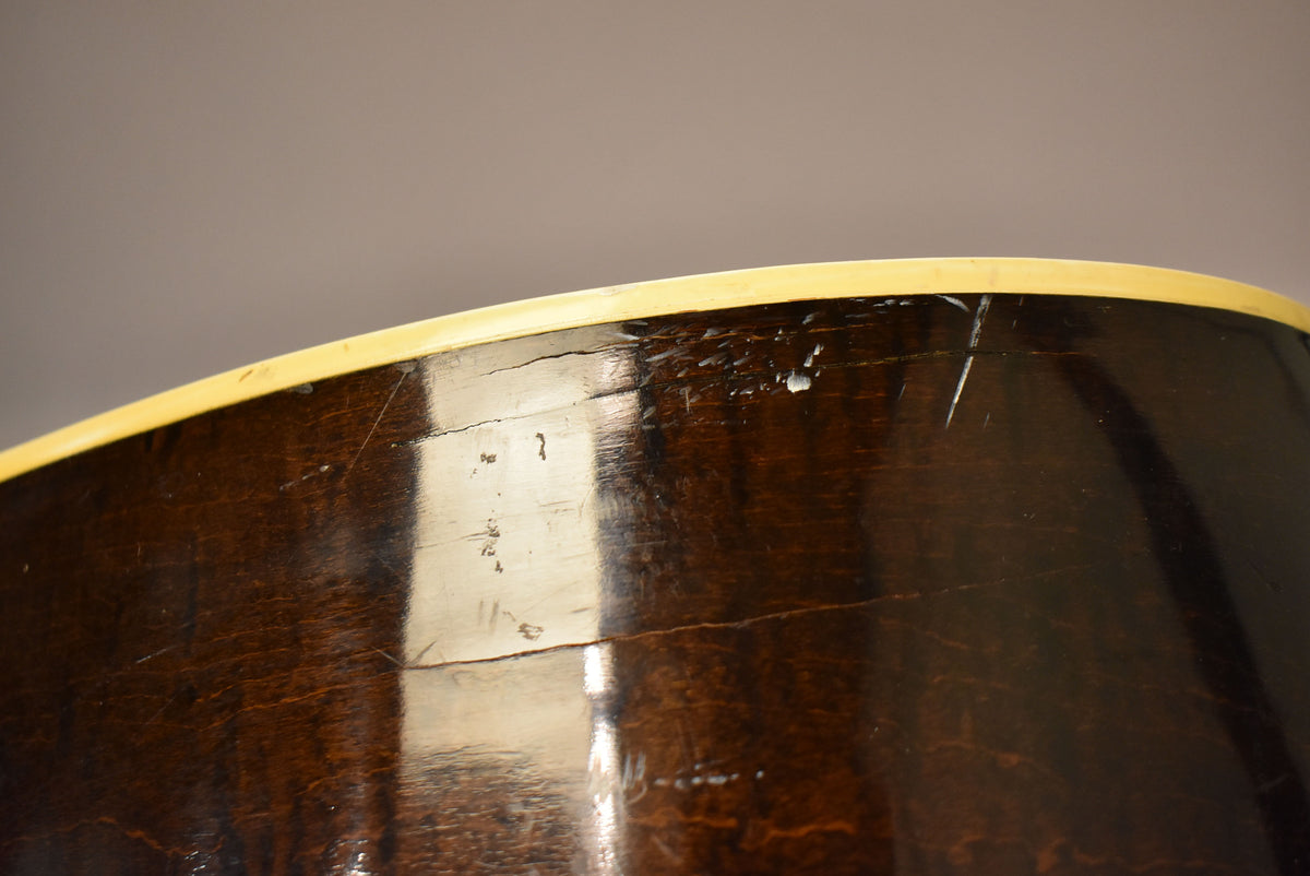 Close-up of the guitar's dark brown side, showing a cream binding, finish checking, scratches, and some chipped areas.
