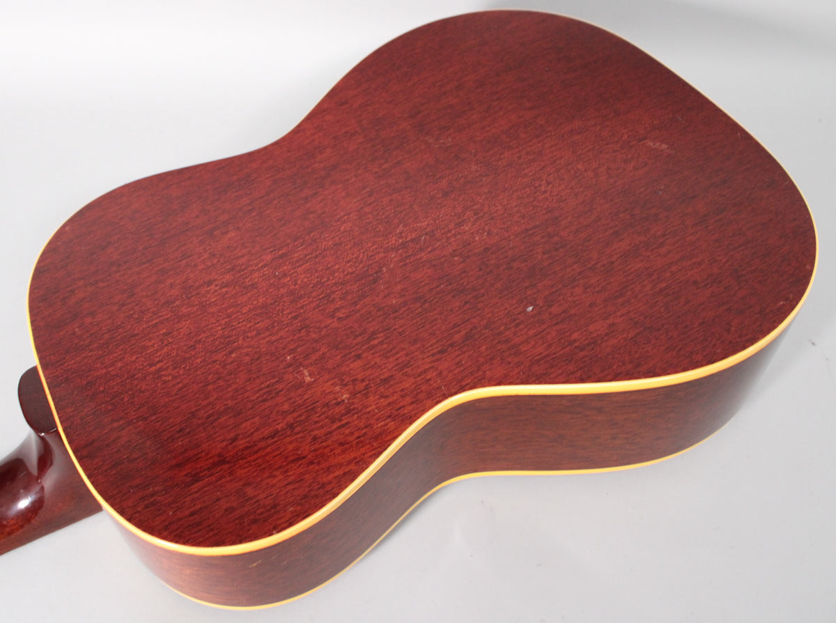The back of the reddish-brown acoustic guitar, showing light wear and a cream binding, with the neck visible on the left.