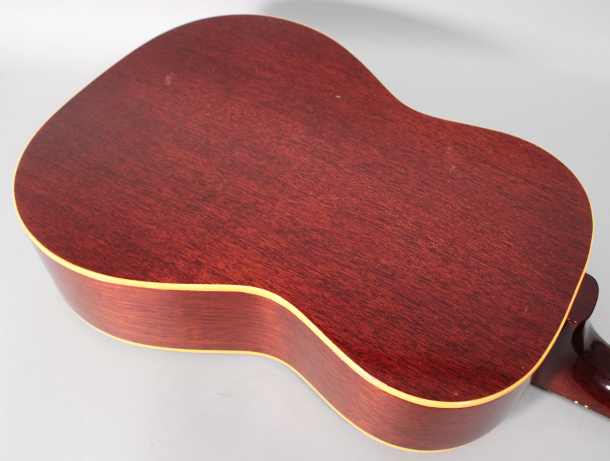 The back of the acoustic guitar, with a dark reddish-brown wood grain and light binding, shows minor scuffs and wear.
