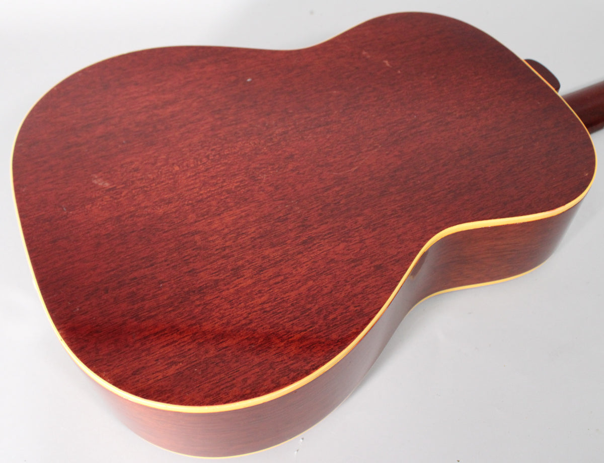 The back of the natural finish acoustic guitar shows a reddish-brown wood grain with light binding and some minor surface wear.
