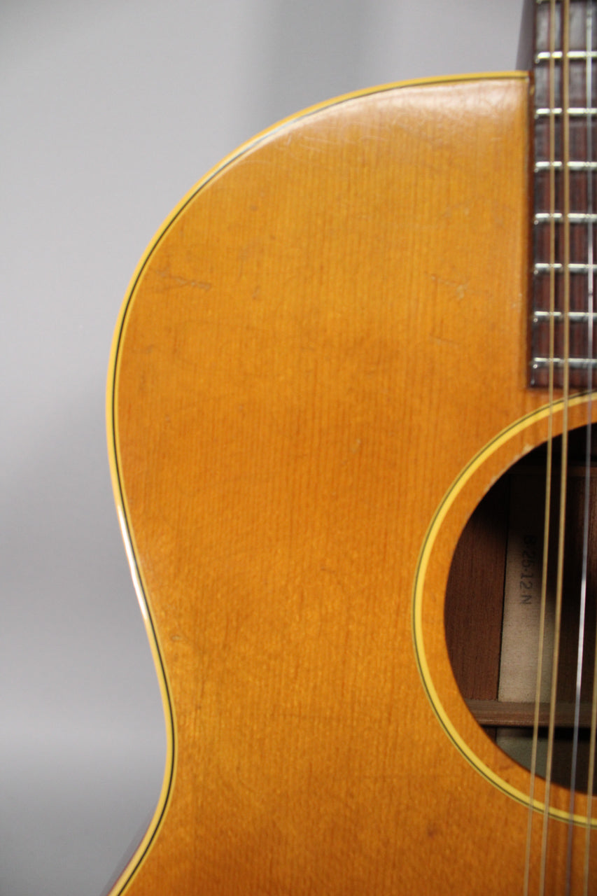 The upper bout of a natural finish acoustic guitar, showing the soundhole, strings, and fretboard, with light wear and checking.