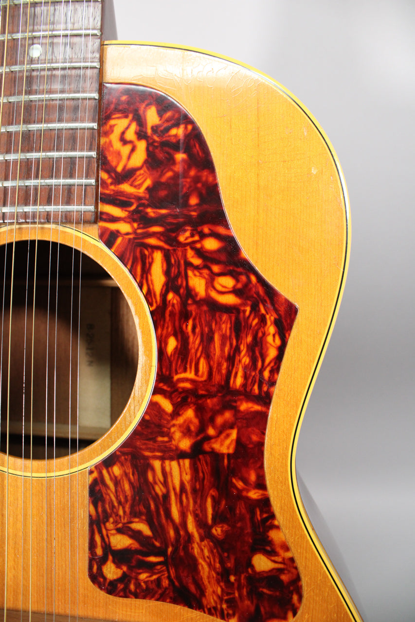 Close-up of the guitar's upper body, showing the natural finish, tortoise pickguard, soundhole, and fretboard with light finish checking.