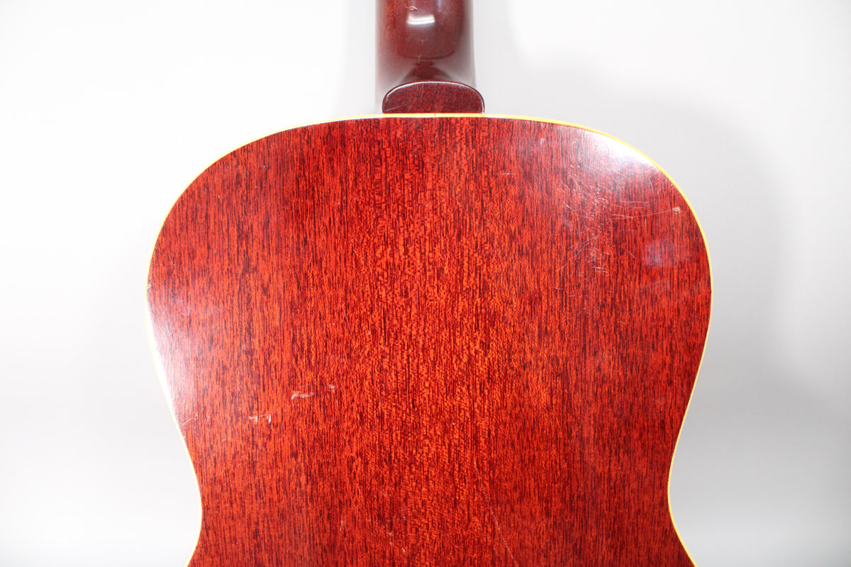 The back of the guitar, showing the reddish-brown wood grain, light binding, and a few scratches and dings on the lower bout.