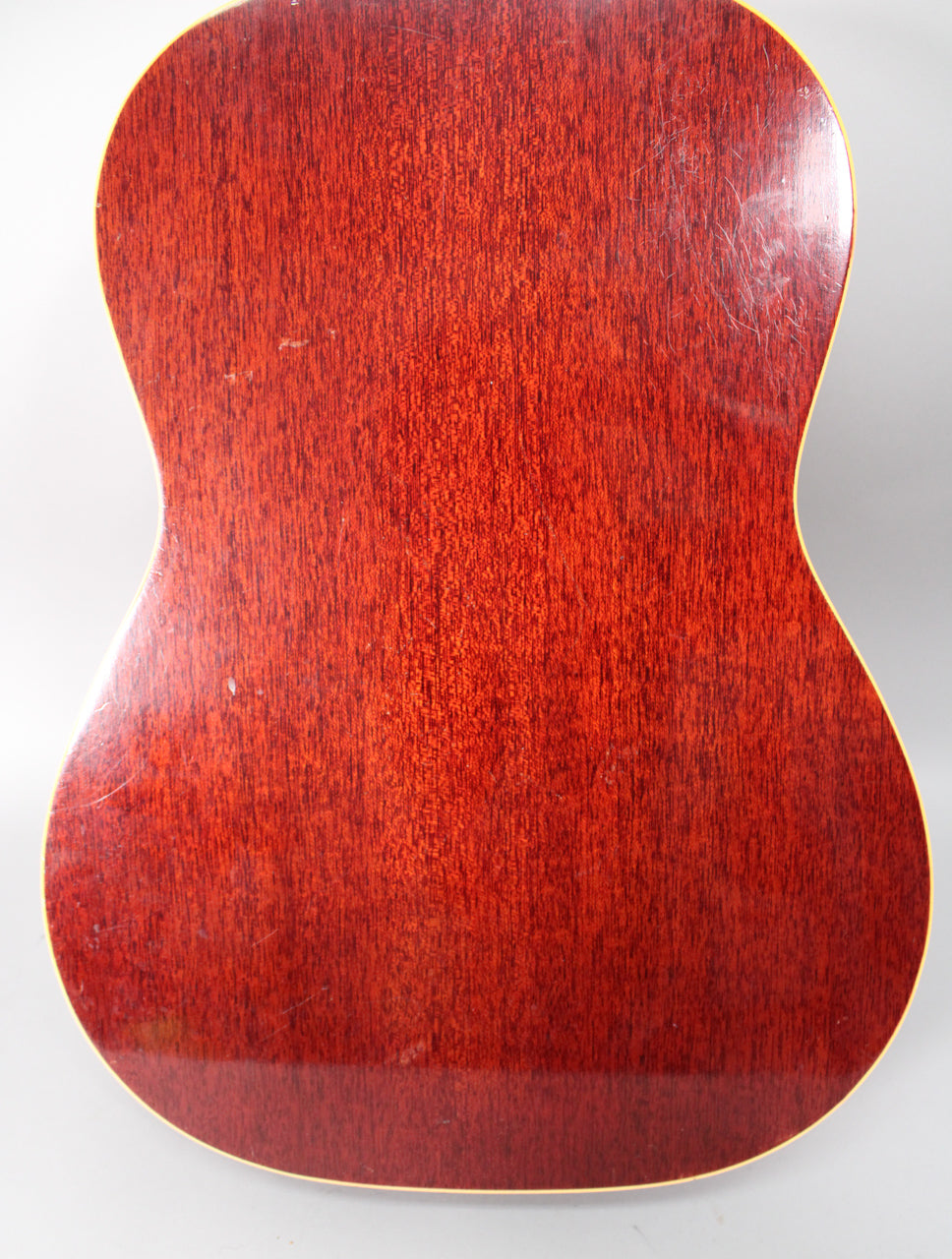The guitar's back, a rich reddish-brown with visible wood grain, shows light scratches and scuffs, framed by cream binding.