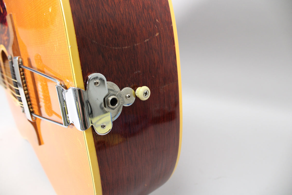 Close-up of the guitar's lower bout, showing the natural finish top, dark brown sides, chrome trapeze tailpiece, and endpin jack.