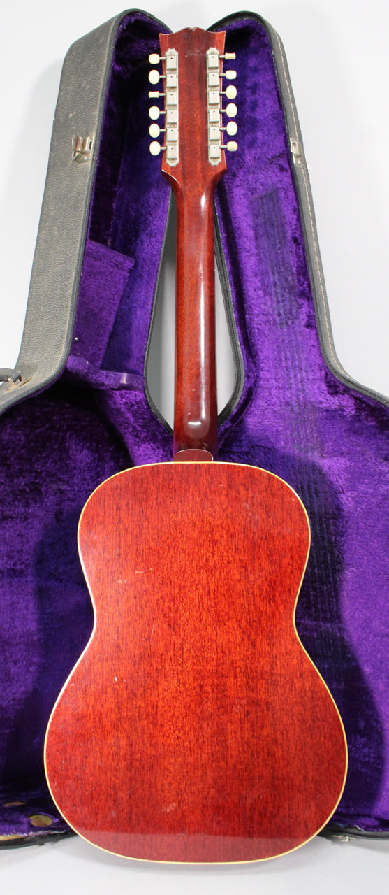 The guitar's back and neck are visible, with a dark red finish and some wear, resting in a black case with purple plush lining.