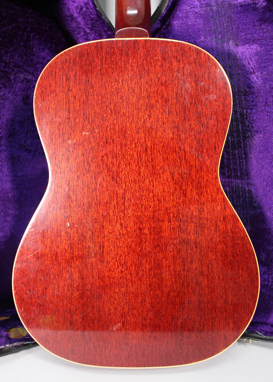 The guitar's back, a rich reddish-brown with visible wood grain, shows light wear and scratches, framed by a purple case.