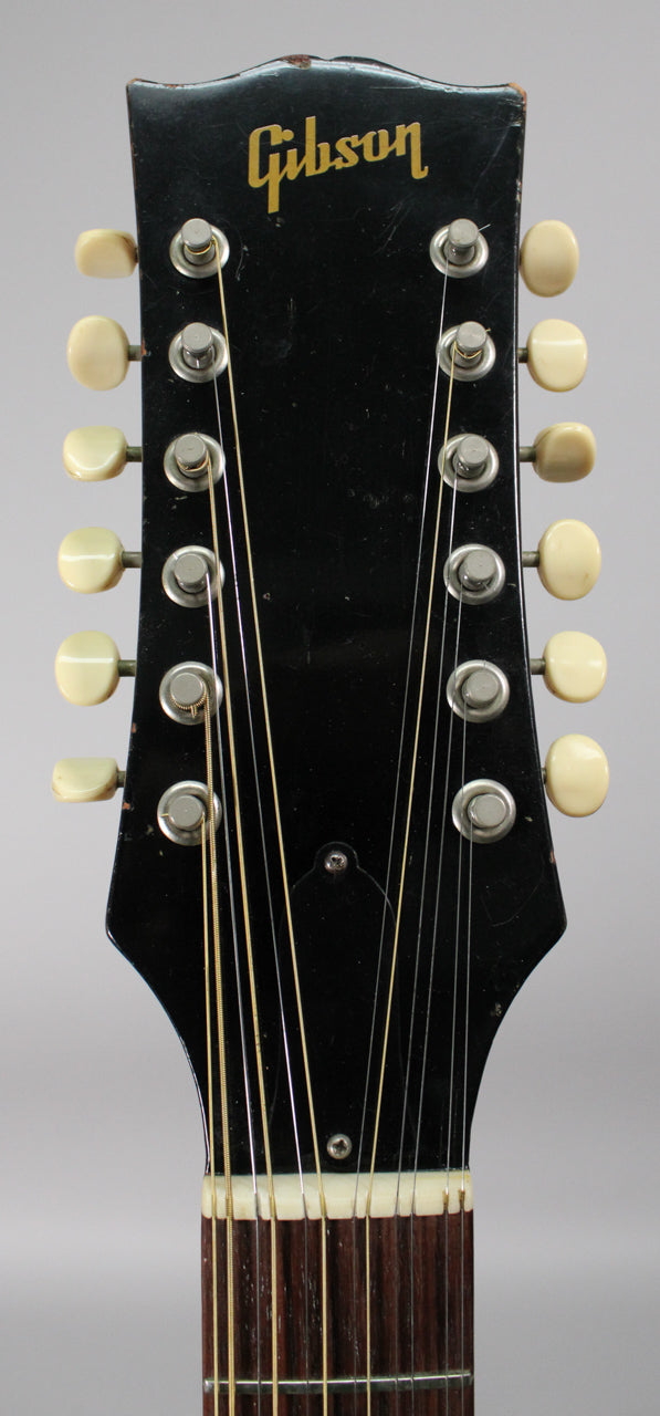 Close-up, top-down view of the black headstock with 12 cream tuning pegs, showing some wear on the edges.