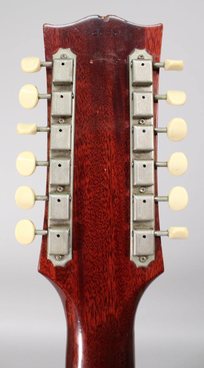 The back of a dark reddish-brown headstock with a serial number stamped at the top, featuring 12 cream-colored tuning pegs.