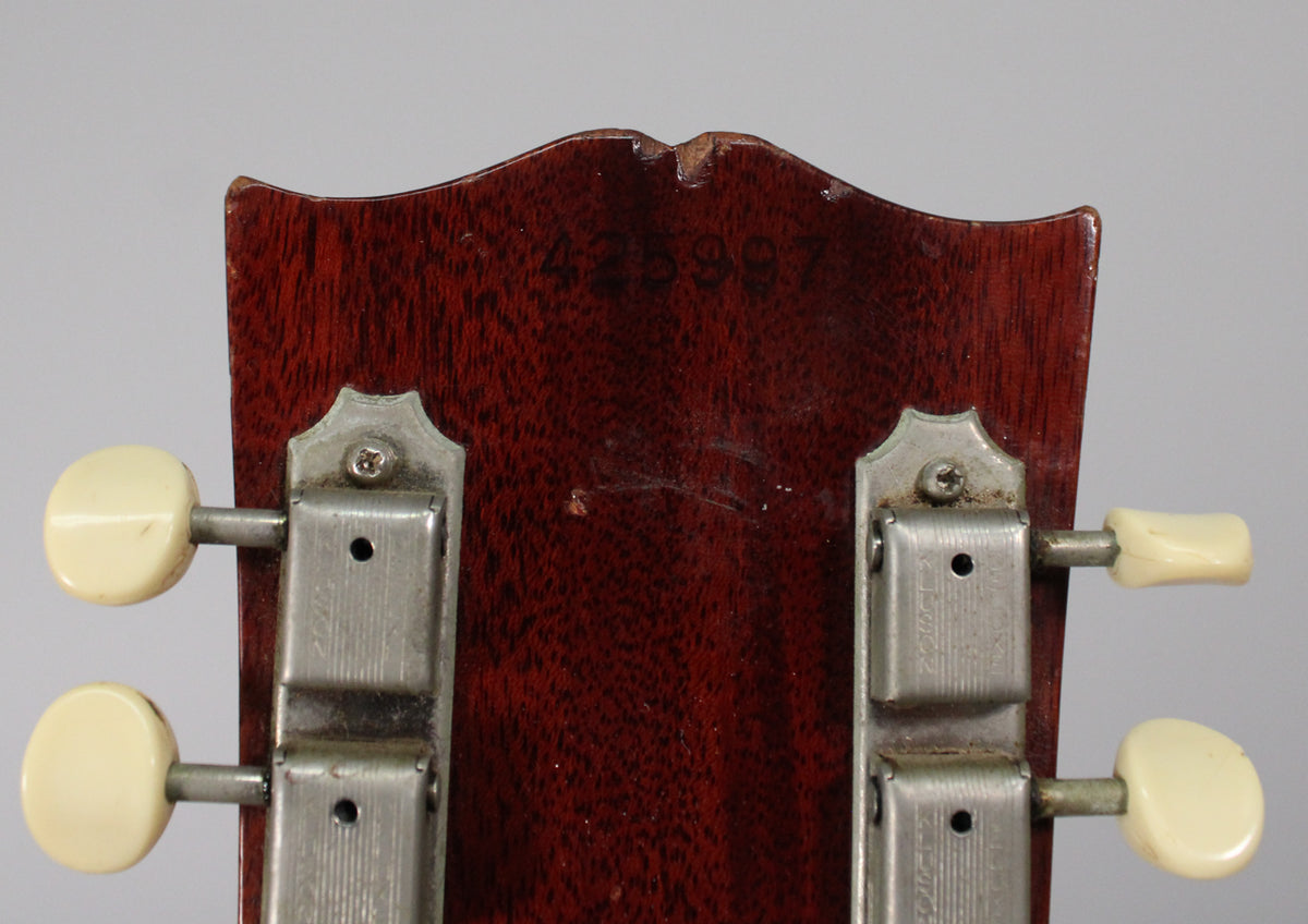 Rear view of the dark reddish-brown headstock, showing two rows of cream-buttoned tuners and a chipped top edge.