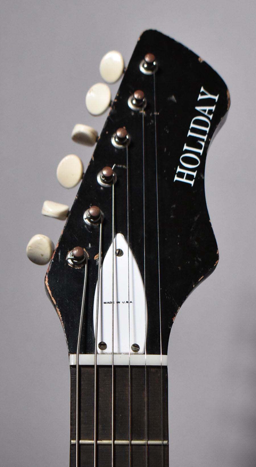 Close-up of the black headstock with white tuning pegs, showing finish wear and a white truss rod cover.