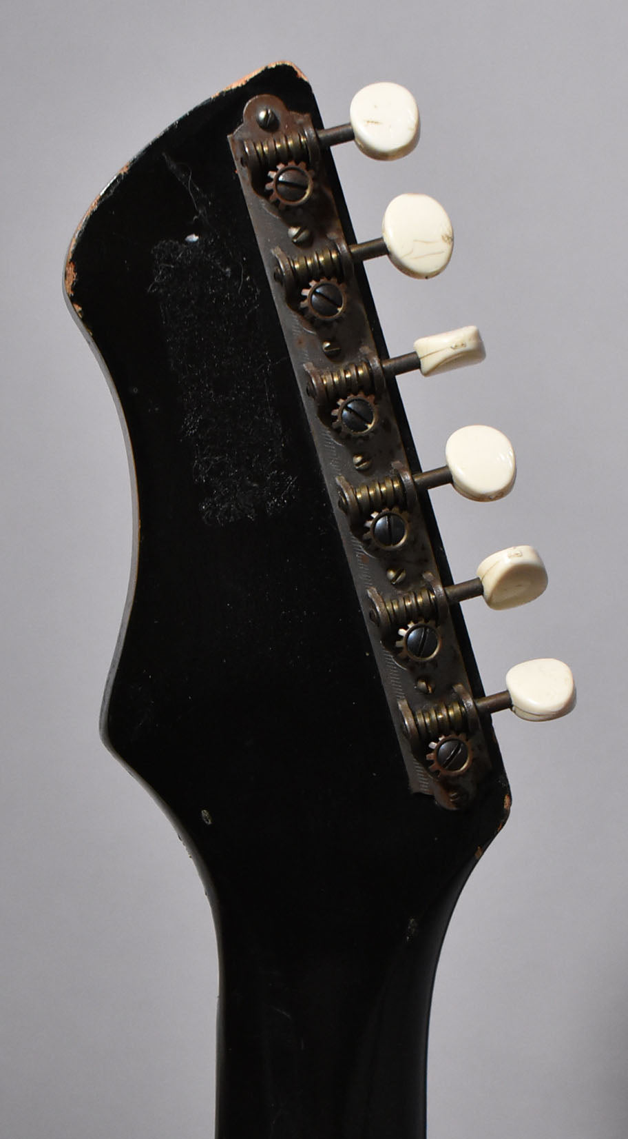 Close-up of the black headstock and neck from the side, showing six cream tuning pegs and tarnished metal hardware.