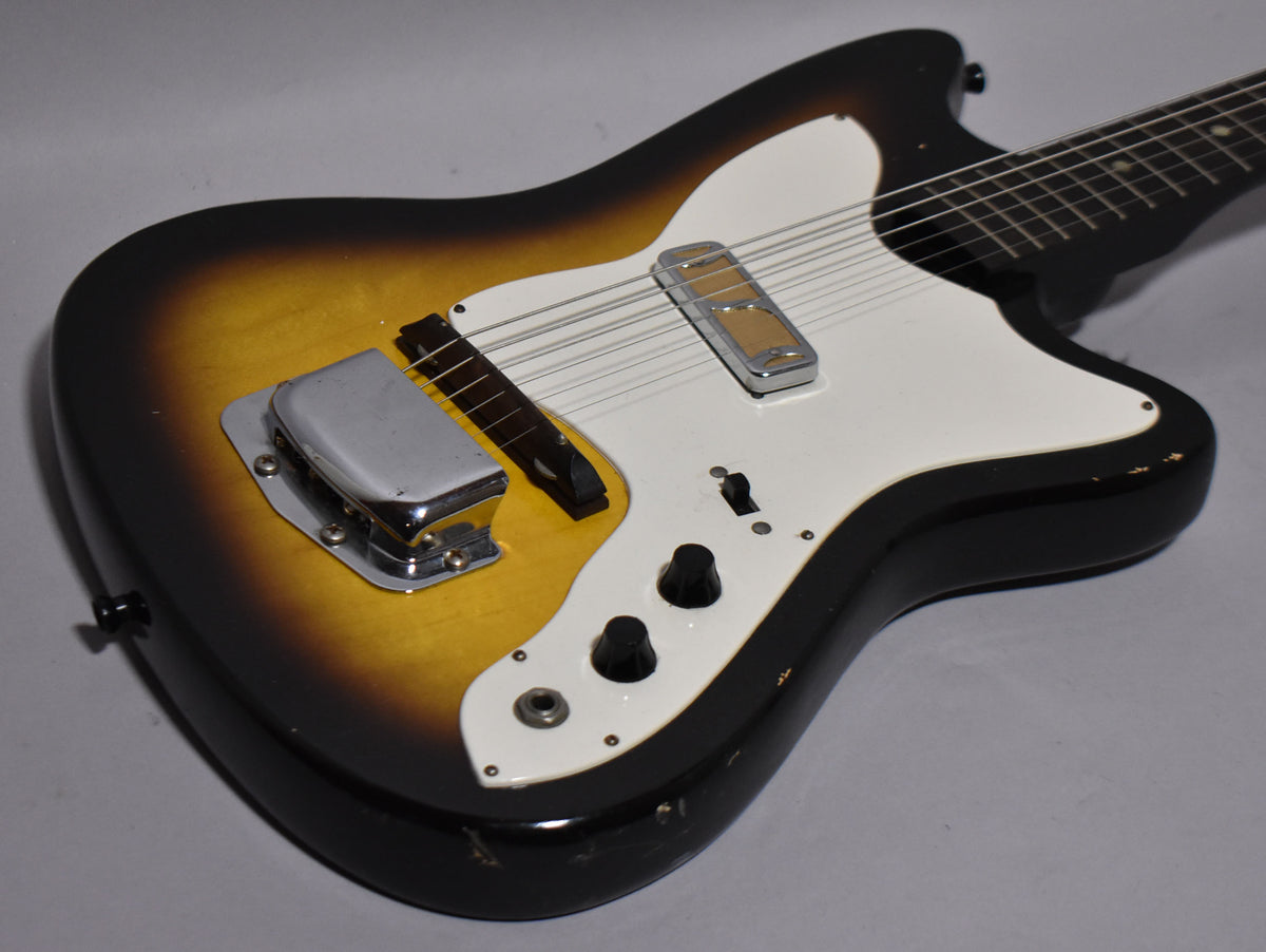 Sunburst electric guitar, angled from above, showing the body, white pickguard, chrome bridge cover, and two black control knobs.