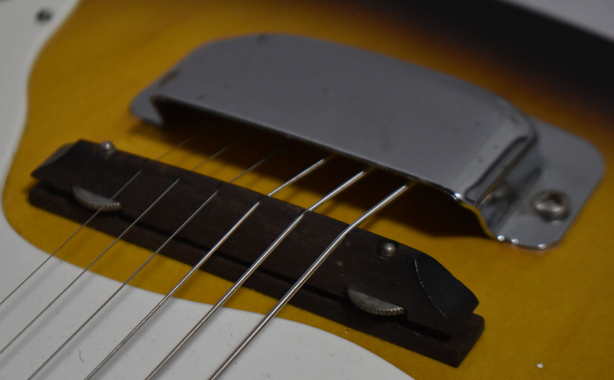 Close-up of the guitar's sunburst body, showing the chrome bridge cover and wooden bridge with visible string wear.