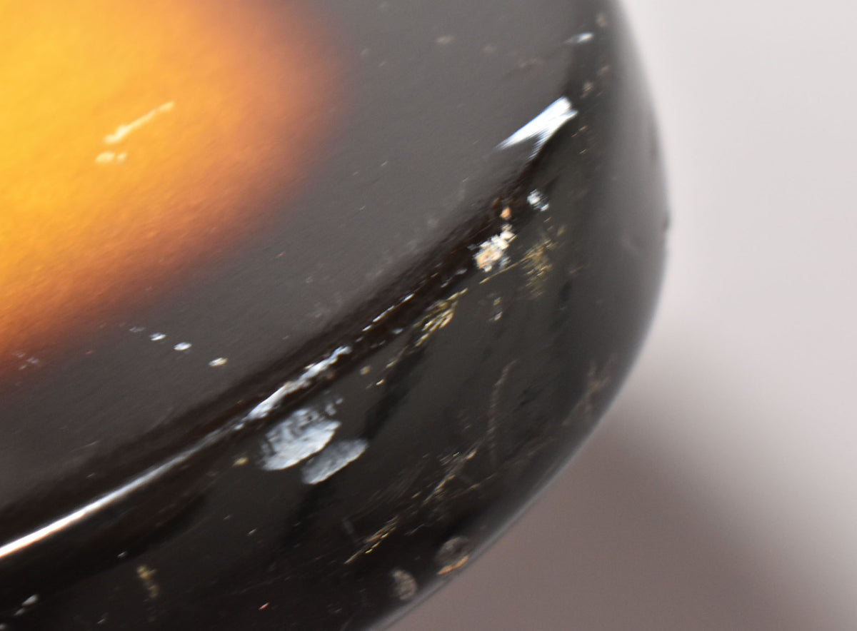 Close-up of the guitar's sunburst body, showing significant paint chips, scratches, and wear along the dark brown edge.