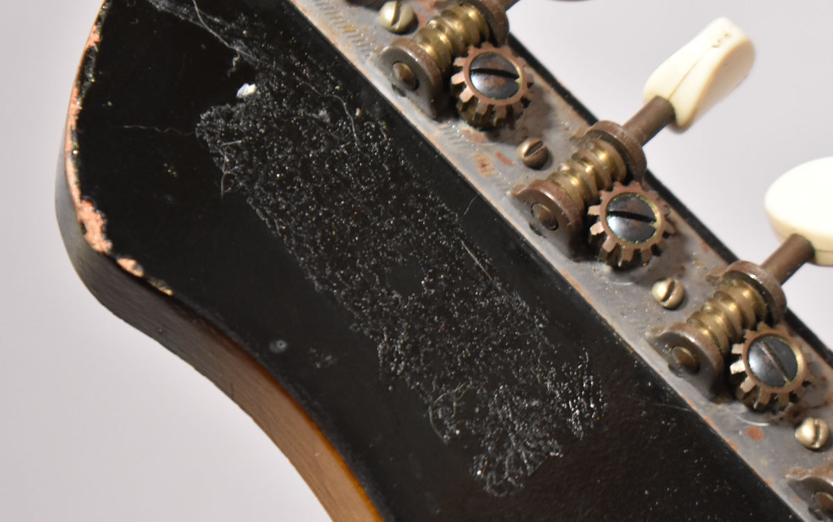 Close-up of the guitar's headstock, showing heavy finish wear, checking, and exposed wood on the black surface, with rusty tuners.