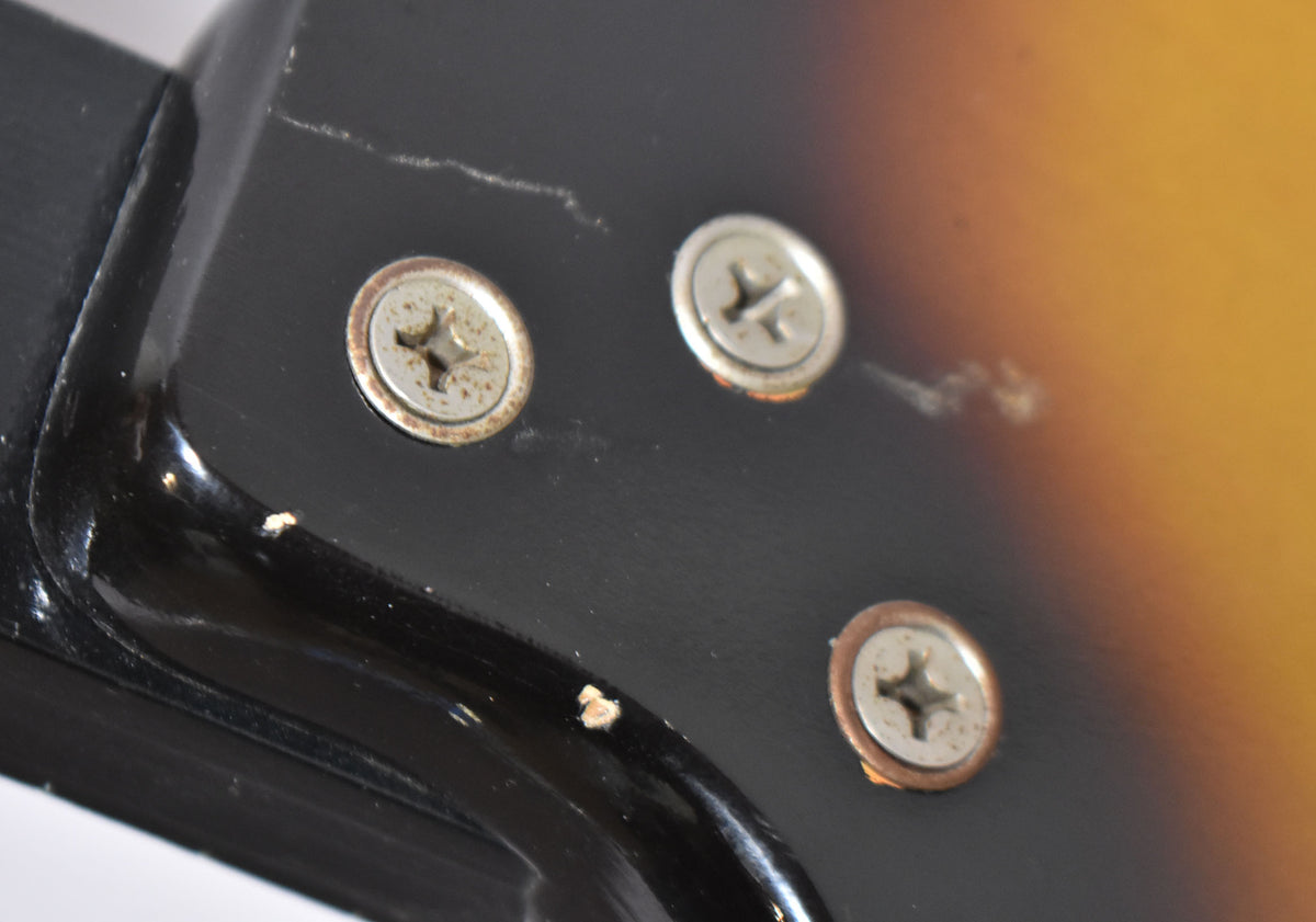 Close-up of the guitar's sunburst body near the neck joint, showing three rusty screws, finish checking, and paint chips.