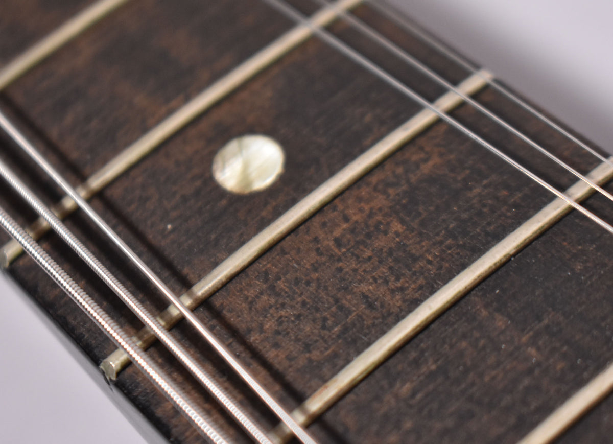 Close-up of the dark, worn fretboard with a single circular mother-of-pearl inlay, showing four strings and light fret wear.