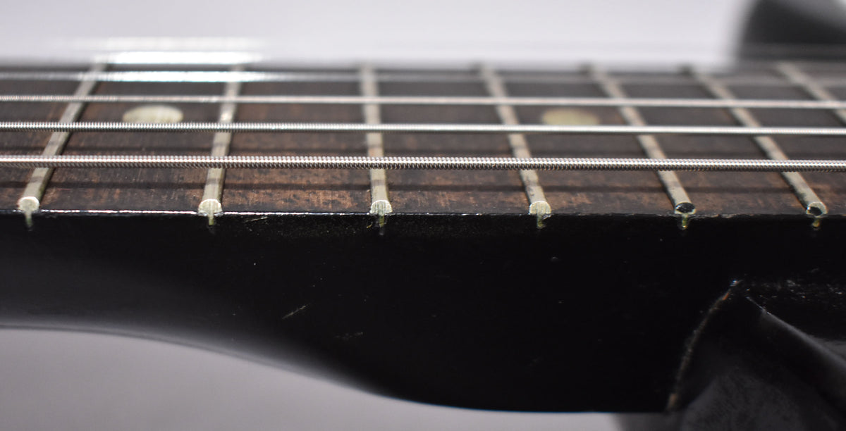 Close-up of the guitar's dark fretboard and frets, showing some wear and light scratches on the black neck finish.