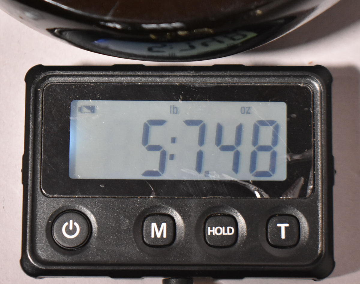 A close-up of a digital scale displaying "5:748" in pounds and ounces, with the guitar's dark body partially visible above.