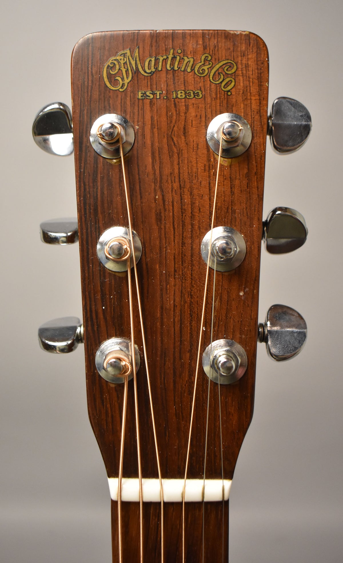 The guitar's dark wood headstock with six chrome tuners and gold lettering shows light wear on the top edges.