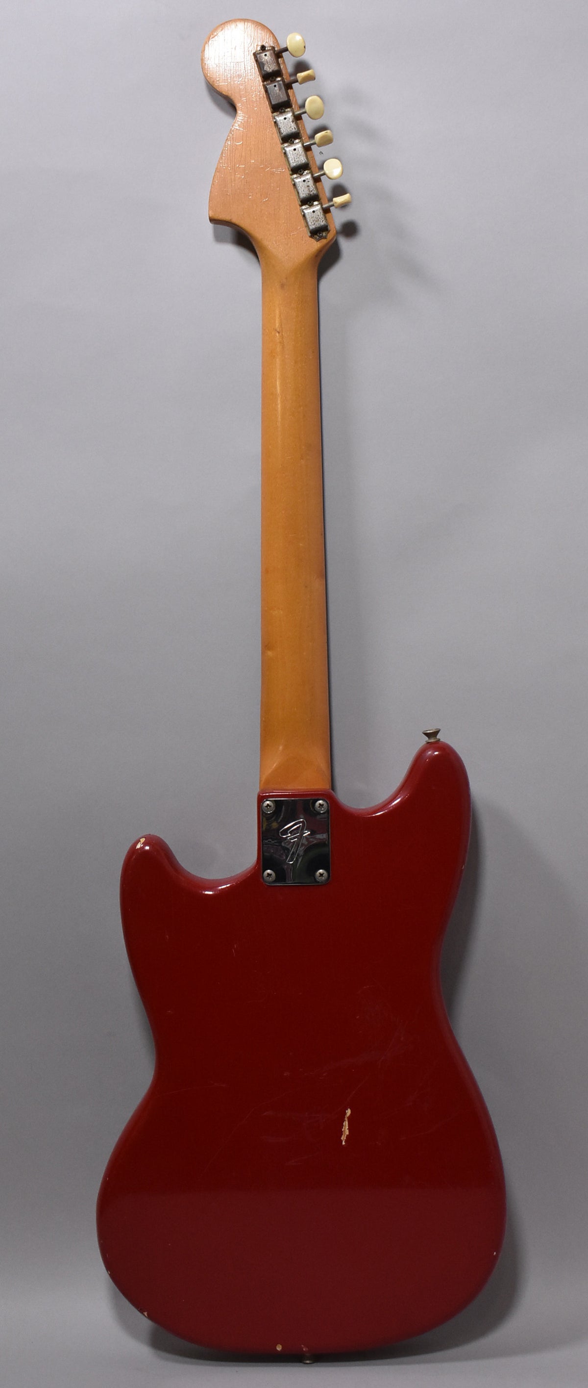 Full back view of the Dakota Red guitar, showing a worn neck plate, six cream tuning pegs, and several chips in the red finish.