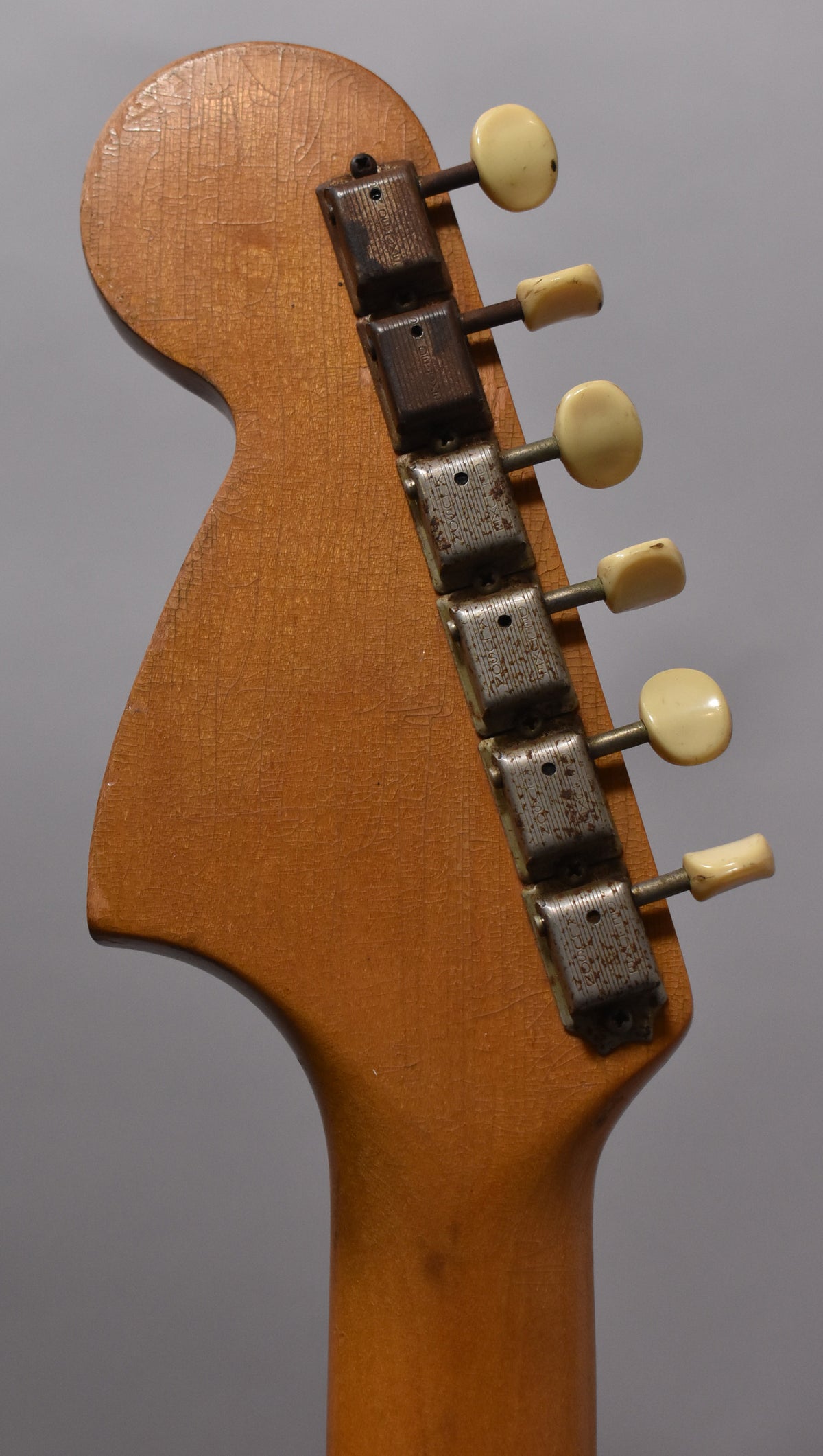 Close-up of the guitar's headstock and upper neck, showing six cream tuning pegs and heavily rusted metal tuners on a crackled, amber finish.