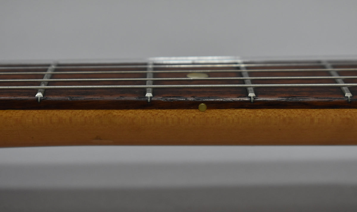 Close-up of the guitar's dark rosewood fretboard and light maple neck, showing wear and a brass side dot marker.