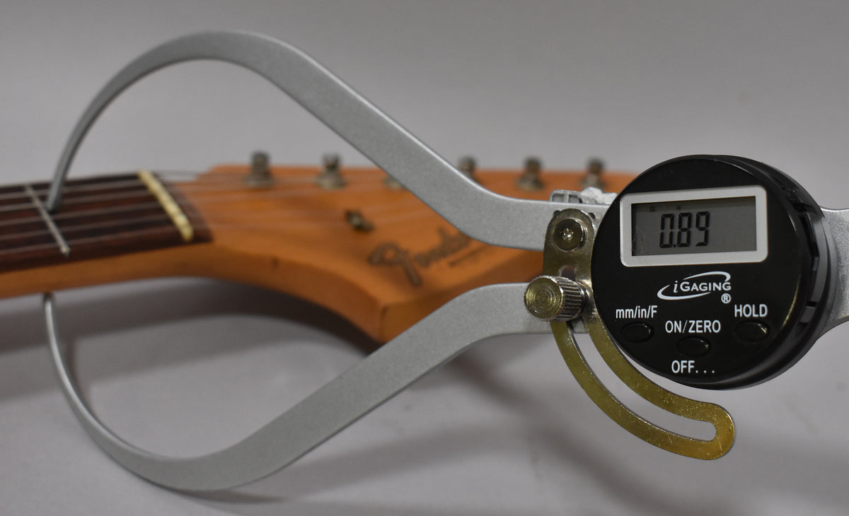 A digital caliper measures the nut width of the guitar's headstock, showing "0.89" on its display.