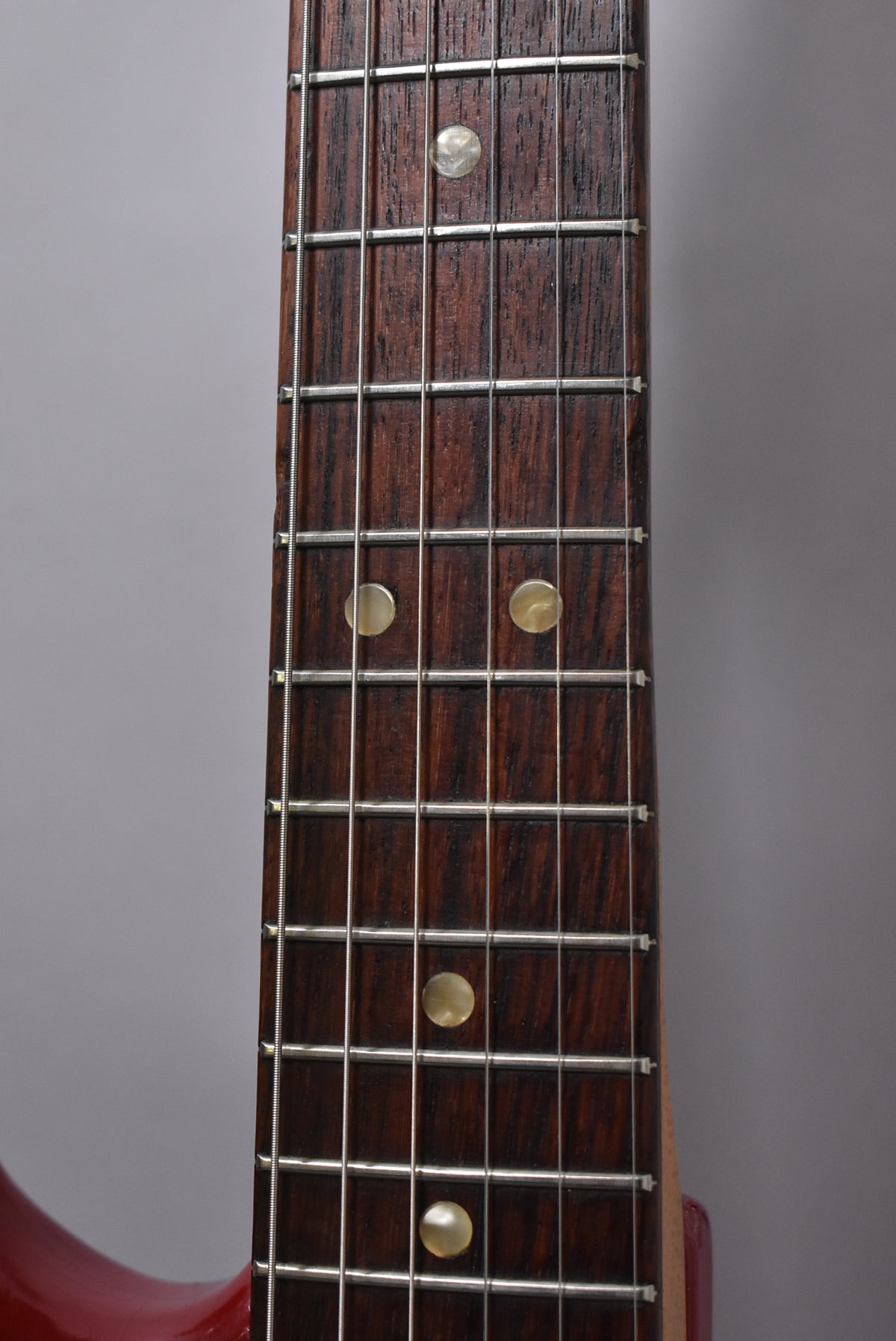 Close-up of the dark rosewood fretboard with 5 frets visible, showing circular pearloid inlays and light fret wear.