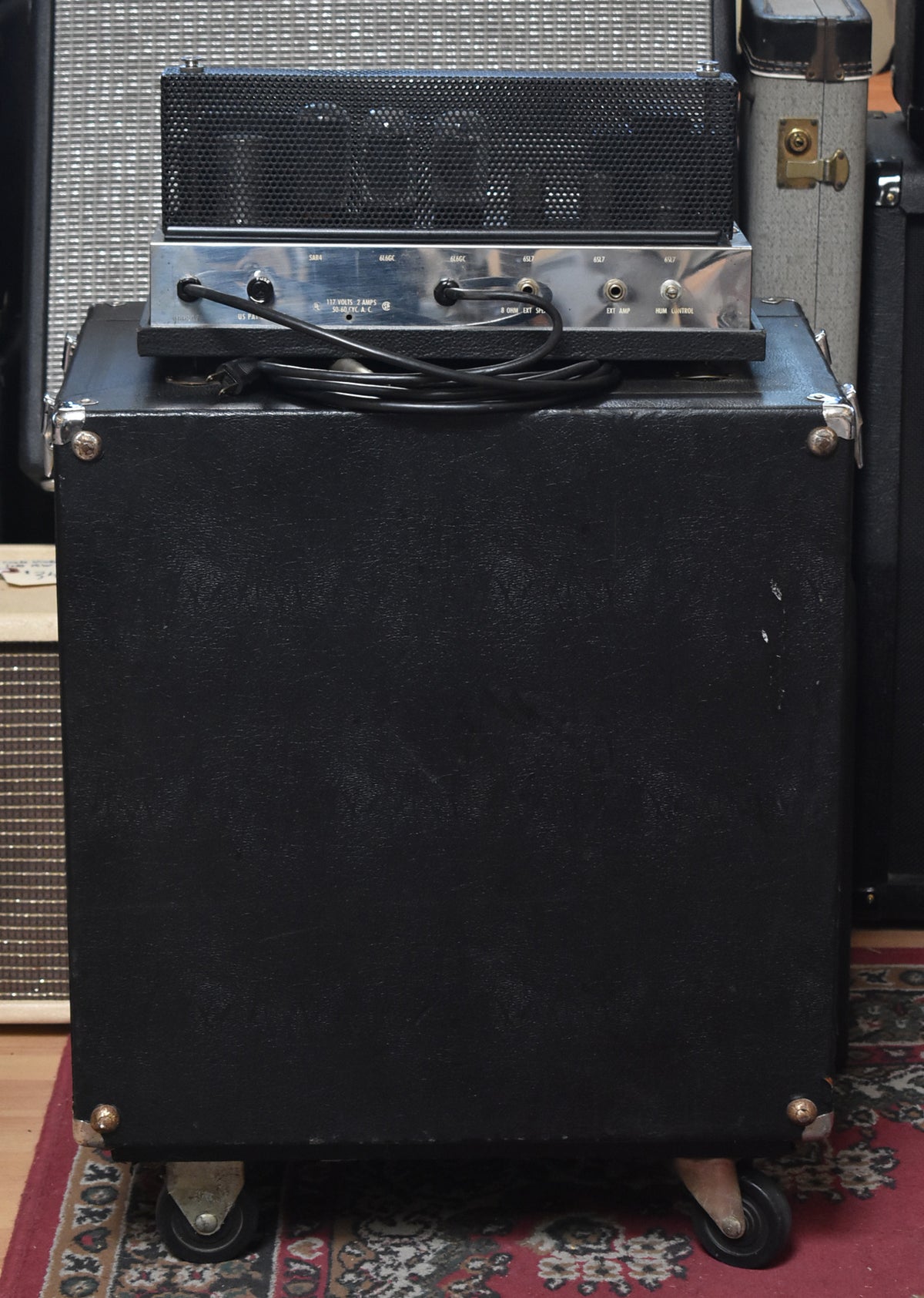 Rear view of the black tolex cabinet with chrome corner protectors and casters, showing the amp head's silver control panel with inputs and power cord.