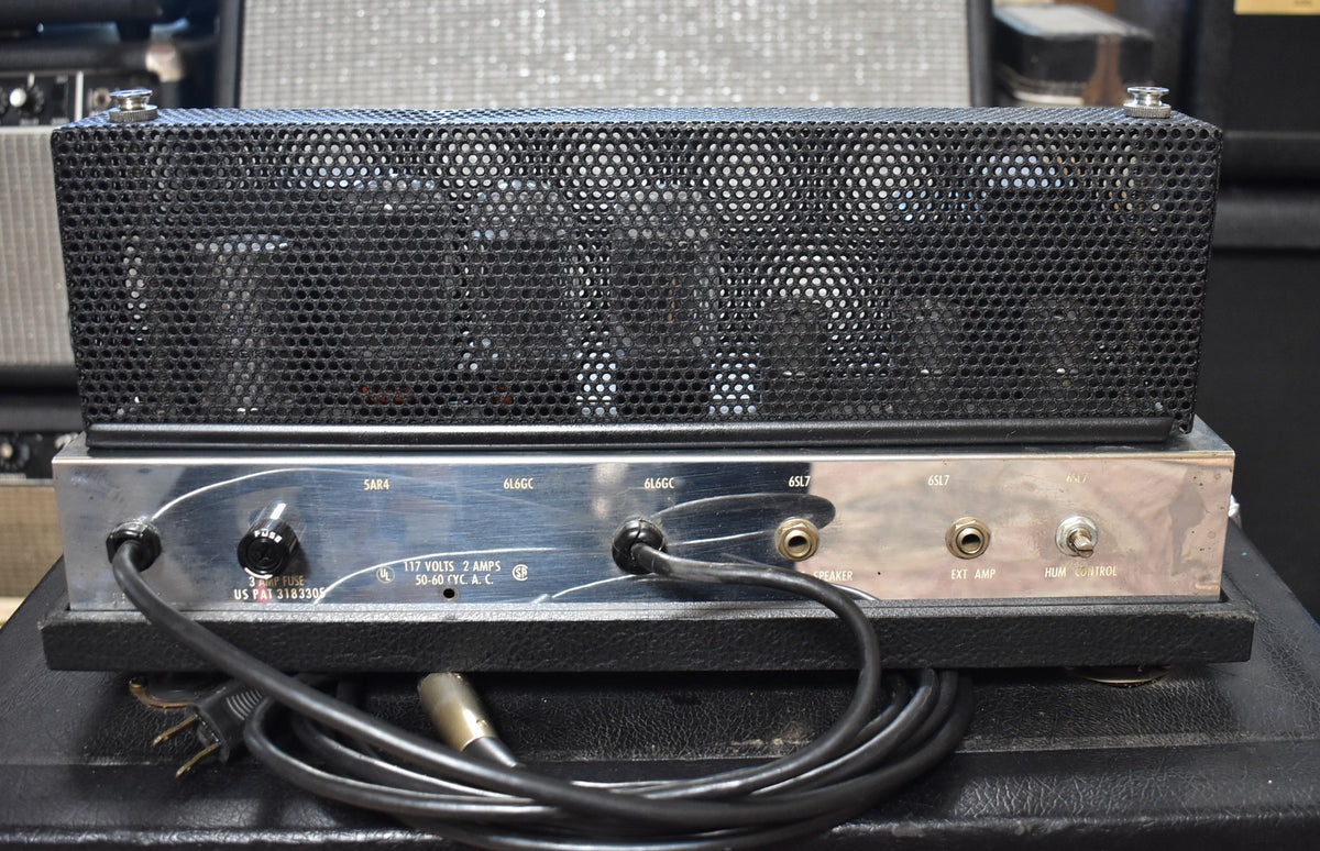 Rear view of the amplifier head, showing the black mesh tube cage, chrome chassis with inputs, and coiled power cable.