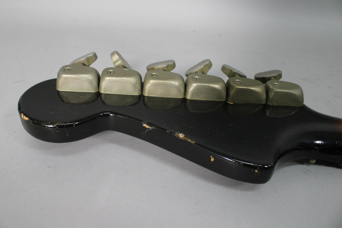 Close-up of the guitar's headstock, showing six rectangular, matte silver tuners and wear on the black finish.