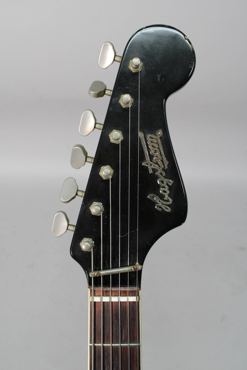 Close-up of the black headstock with six chrome tuners, showing finish wear on the top edge and a string retainer bar.