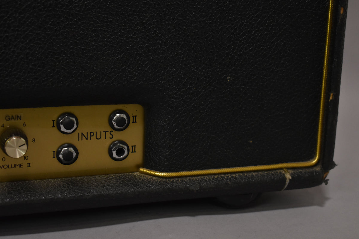Close-up of the black tolex amp's lower right, showing the gold control panel with four inputs, a Gain knob, and worn gold piping.
