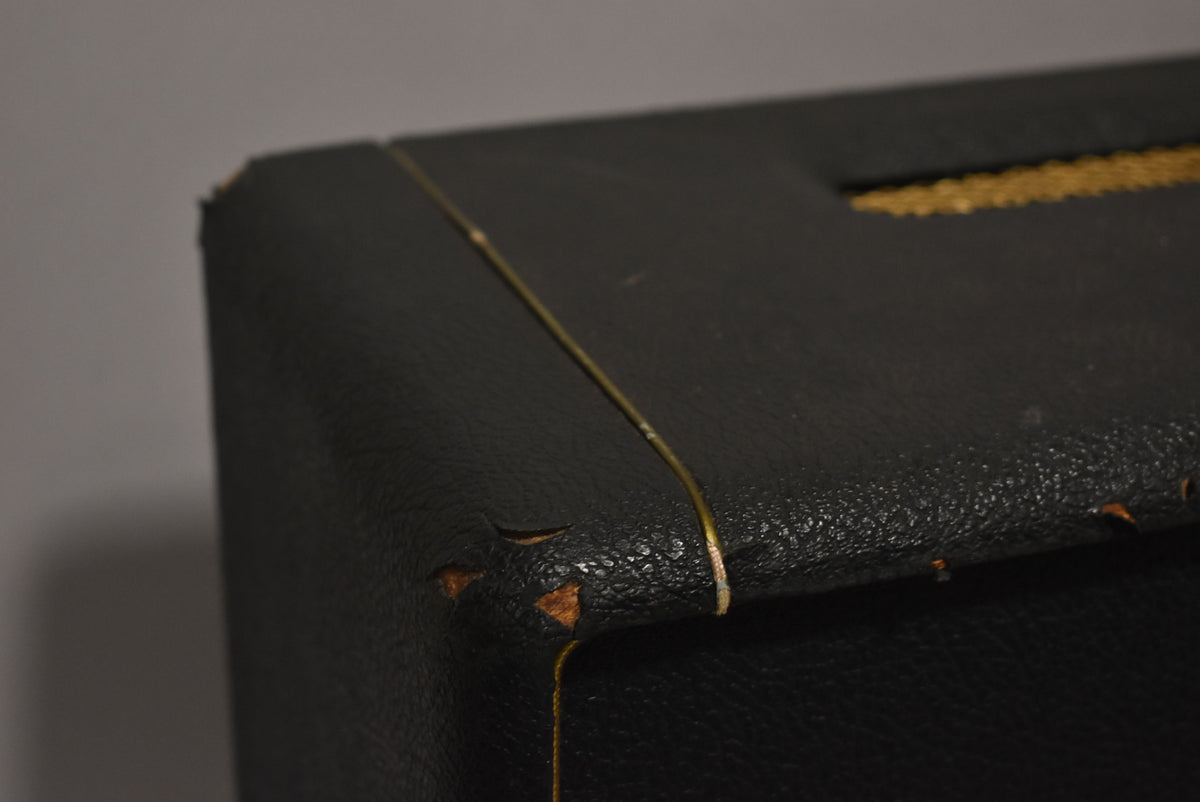 Close-up of the amplifier's top left corner, showing black textured tolex with worn edges revealing wood and a thin gold piping.