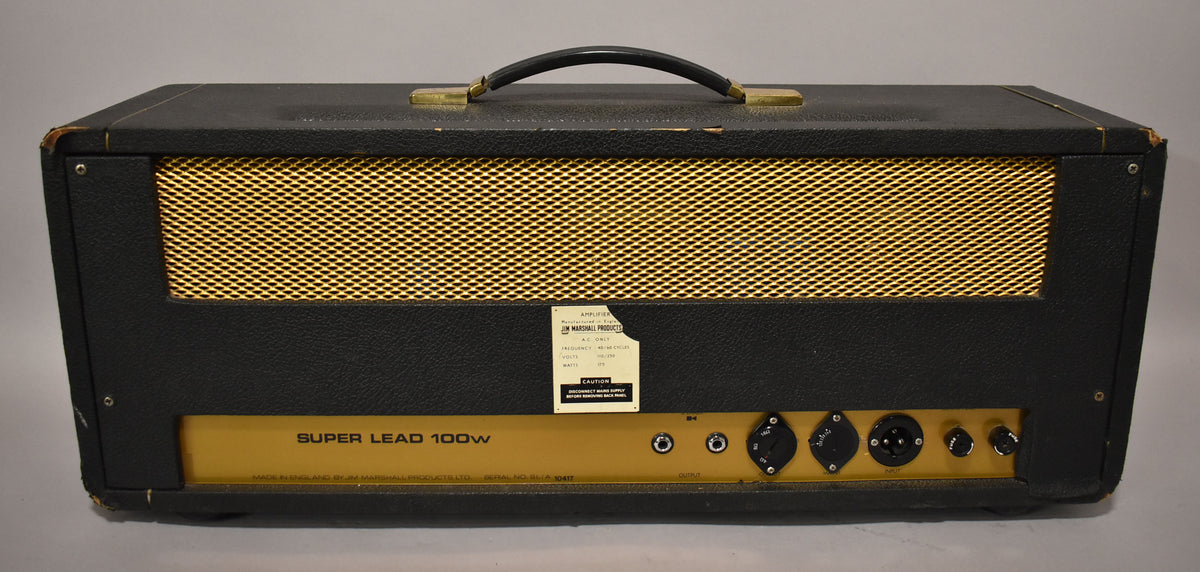 Rear view of a black amplifier head with a gold mesh vent, a gold control panel with various inputs, and a black handle.