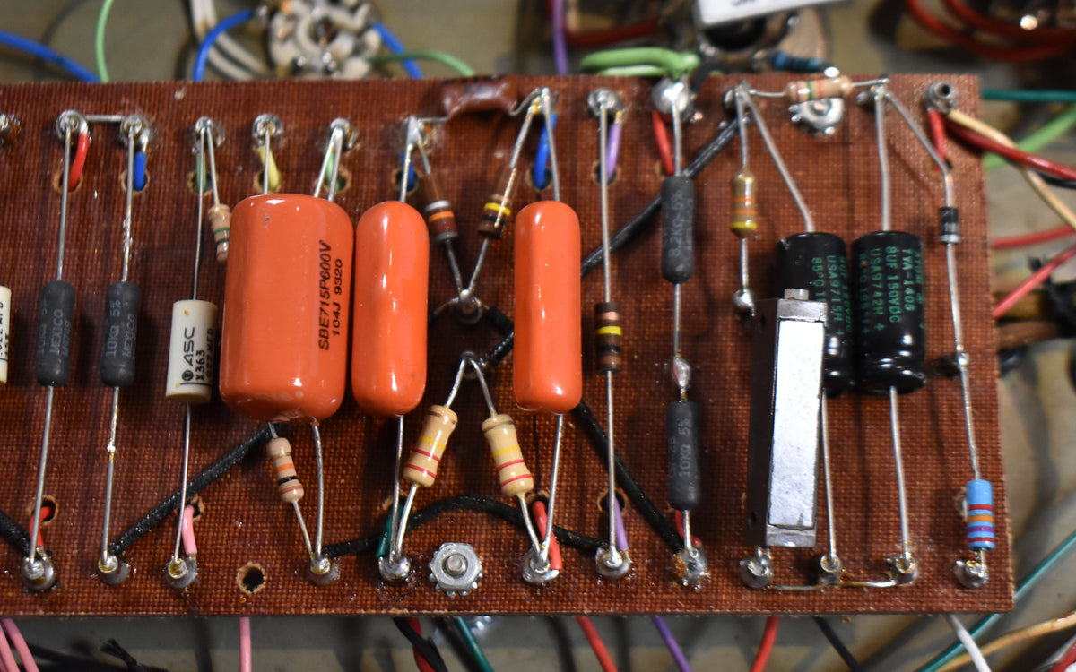 Close-up of the amp's brown circuit board, showing orange capacitors, various resistors, and black and silver components.