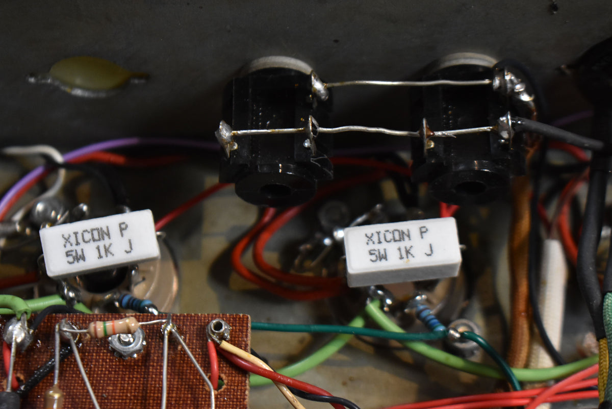 Close-up of the amp's internal wiring, showing two black input jacks, two white ceramic resistors, and a brown circuit board.